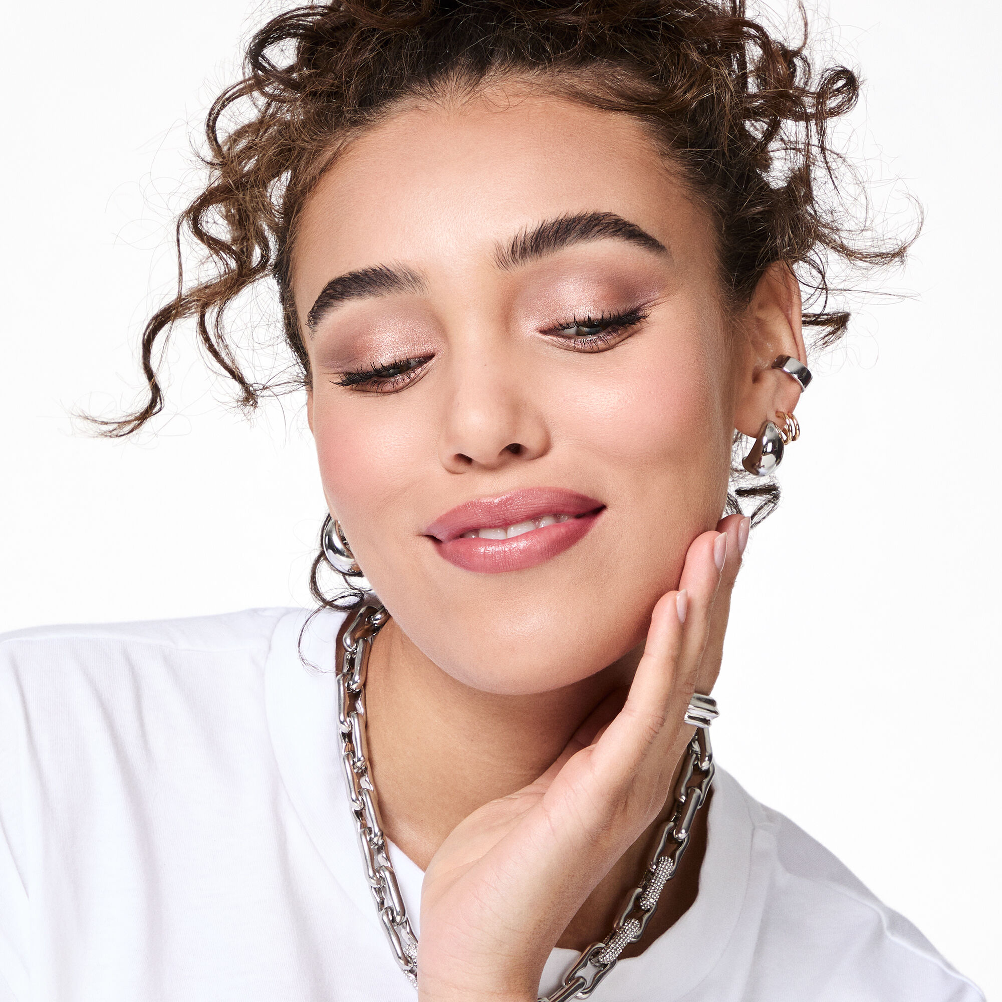 A brunette model with curly hair wearing the All Eyes on Hue look soft smiles while looking down.