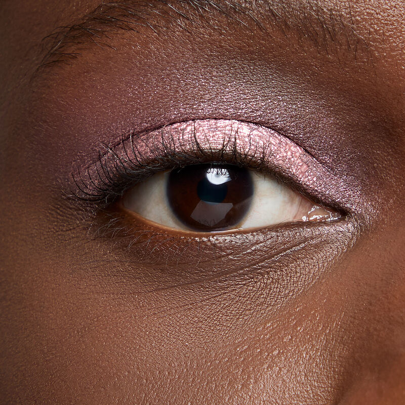 A model with a deep skin tone and brown eyes wears shade Pink Prisms.