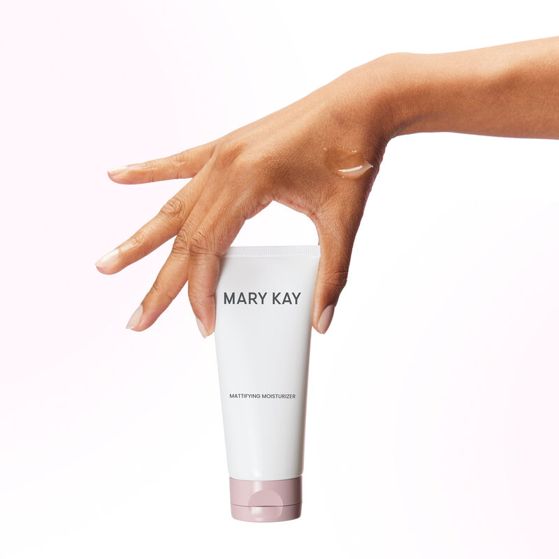 Hand with splayed fingers holding tube of Mary Kay Mattifying Moisturizer with product rub on the hand